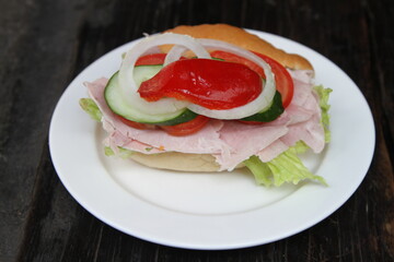 German bread roll with cooked ham, lettuce, tomato, bell pepper and onions
