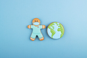 the gingerbread man is a doctor in medical mask and blue uniform with a gingerbread planet earth. the concept of a global coronavirus pandemic, thanks to the doctor