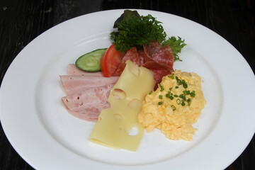 German breakfast with scrambled egg, cold cuts, cheese, lettuce, tomato and cucumber