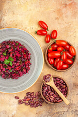 Vertical view of delicious salad with beetroot and bean and beans inside and outside of pot and tomatoes on mixed color table