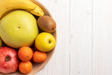 Wooden bowl with different fruits on white table. Top view, close up.