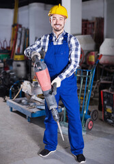 Young positive man worker practicing jackhammer for construction work at workplace.