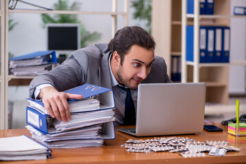 Young male sick employee suffering at workplace
