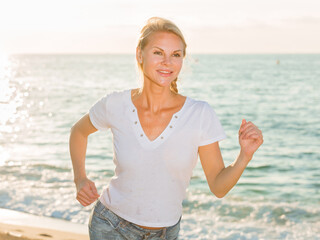 Female in white T-shirt is jogging on the beach.