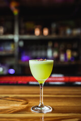 A light green sour tequila cocktail in a nick and nora glass, radish chips garnish