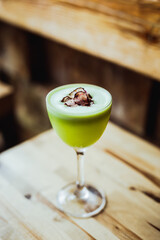 A light green sour tequila cocktail in a nick and nora glass, radish chips garnish, on a wooden table, 45 degrees angle shot