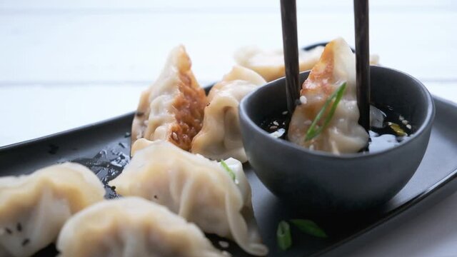 Fried gyoza dumplings with sauce and green onions on black plate, dark background. Japanese cuisine concept.