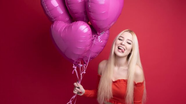 Stop motion. Happy blonde with a heart-shaped balloon in the form of a heart in her hands. Red isolated studio background.