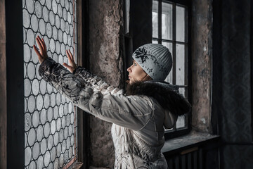 A beautiful girl stands near a stained glass window in an abandoned house. Girl in a white jacket and hat. Beautiful interior of an abandoned manor. Light through the windows.