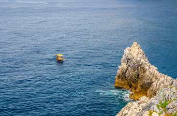 Yellow boat on blue dark water of Grotta di Lord Byron near coast with rock cliff, Portovenere...