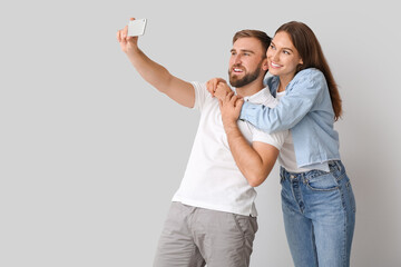 Fototapeta premium Young couple taking selfie on light background