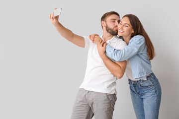 Fototapeta premium Young couple taking selfie on light background
