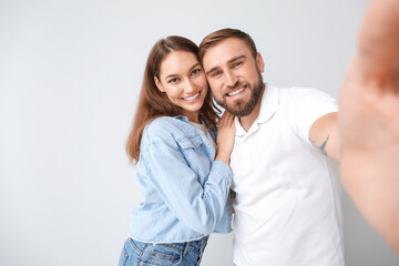 Young couple taking selfie on light background