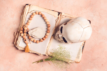 Spell book, human skull and beads on color background