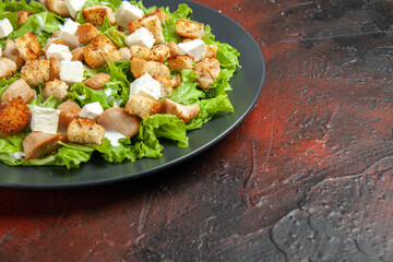 bottom half view caesar salad on oval plate on dark red background