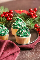 Plate with tasty Christmas cupcakes on table