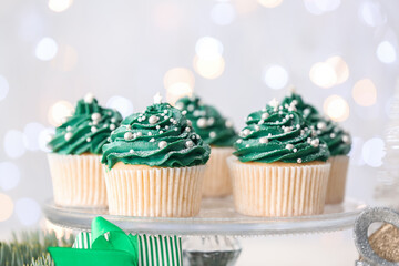 Stand with tasty Christmas cupcakes on light background