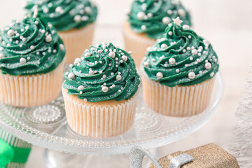 Stand with tasty Christmas cupcakes on light background