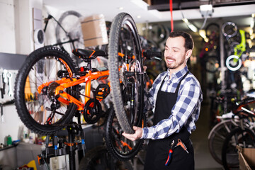 Fototapeta na wymiar Worker in apron shows structure of bicycle wheel in sporting goods shop