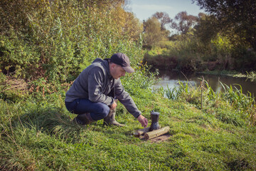 Man sits on the grass and makes coffee over the fire. Tourism near the river. Male tourist brews coffee on the fire.