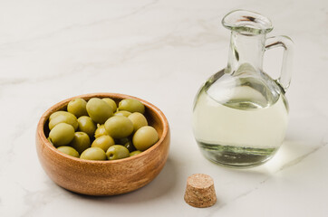 Bottle of olive oil and olives in a wooden bowl. Olive oil bottle and olives on white stone table