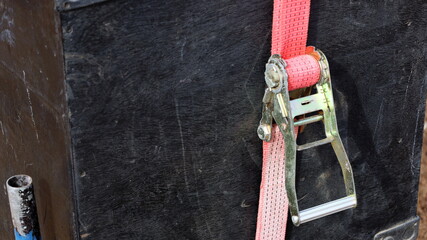 Red ratchet strap. Close-up ratchet tie down secures stacked black speaker cabinets.