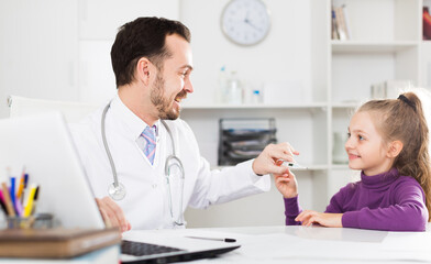 Fototapeta premium Little smiling girl visiting consultation with man doctor in hospital