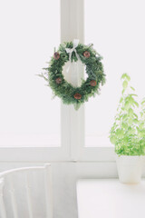 simple DIY green Christmas fir wreath with cones hanging on white window. Rustic lifestyle home interior.