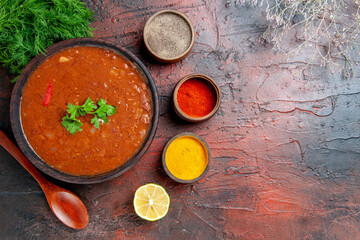 Above view of classic tomato soup in a brown bowl and different spices on mixed color table