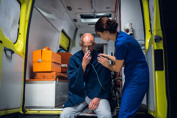An injured, shocked man sitting with an oxygen mask in an ambulance, a medical worker is taking...