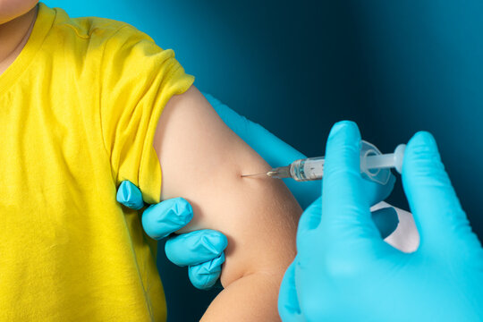 The doctor or nurse injects a syringe to a small child intramuscularly on a blue background. Tuberculosis vaccination, BCG vaccine