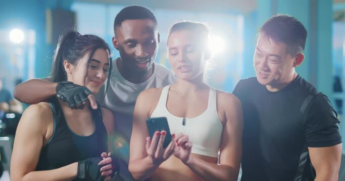 Multi-cultural four friends athletes using smartphone mobile application together while working out at the gym. Team sports. Sportsmen and sportswomen.