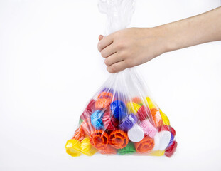 Child's hand holds a package with plastic bottle caps on a white background. Ecology and recycling concept.
