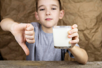 The boy holds a glass of milk and shows a bad thumb sign.