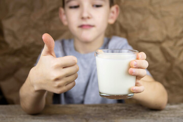 A boy in a gray T-shirt holds a glass of milk. The child shows that milk is good.