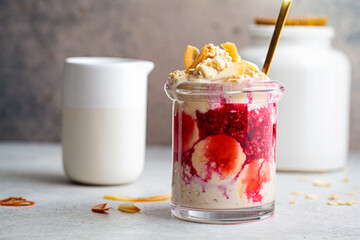 Overnight oatmeal with banana, berry jam and coconut in glass jar.