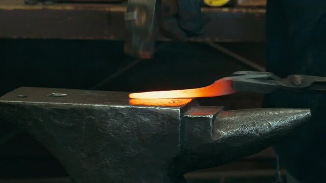 Slow motion close up of blacksmith forge hammering on hot glowing metal in a workshop.