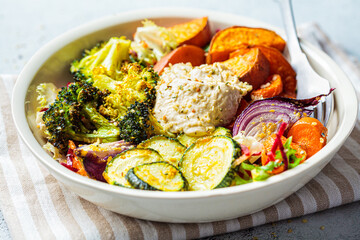 Baked vegetables with hummus bowl. Salad with baked sweet potato wedges, zucchini, broccoli and hummus. Vegan food concept.