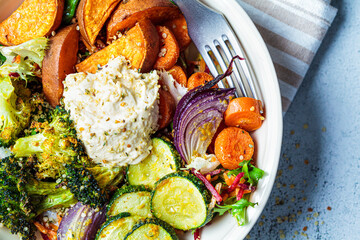 Baked vegetables with hummus bowl. Salad with baked sweet potato wedges, zucchini, broccoli and hummus, top view. Vegan food concept.