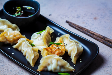 Fried gyoza dumplings with sauce and green onions on black plate, dark background. Japanese cuisine...