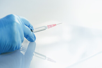 Doctor's hand with glass syringe with a needle on blue. copy space. Medication safe consumption and treatment, vaccine and immunization. Health and pharmacy and vaccination concept banner