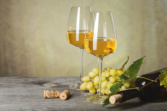 White wine in glasses, wine bottle and grapes on an old wooden table.
