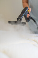 Woman with steam generator cleans bed. Vertical