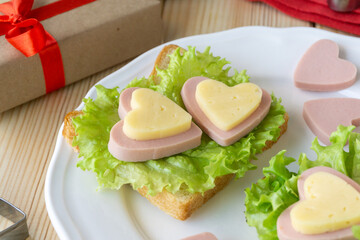 Breakfast for valentine's day. Sandwich with sausage, cheese and lettuce on white plate