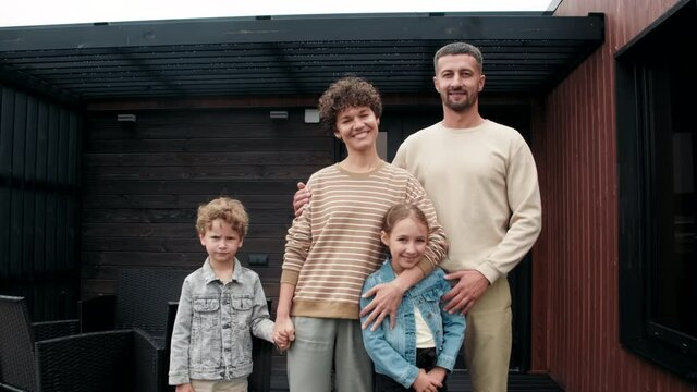 Portrait slowmo shot of happy parents and children posing for camera in front of their house
