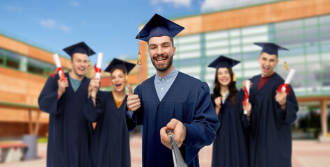 education, graduation and people concept - happy smiling male graduate student in mortar board and bachelor gown taking picture with selfie stick over school background