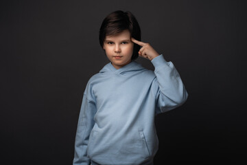 Studio shot of boy 10-12 years old pointing with finger at head. Concept of thinking. Studio shot, gray background