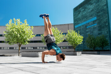 fitness, sport, training and lifestyle concept - young man exercising and doing handstand outdoors