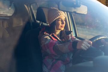 A young smiling woman with hat is driving a car.