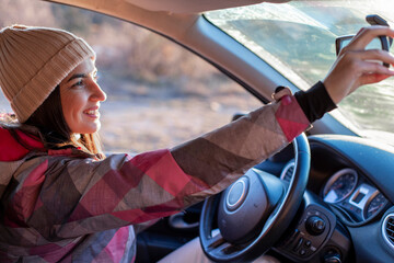 A young smiling woman in winter clothes is driving a car.